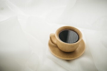 a cup of coffee stands on the windowsill with white curtains
