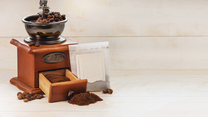 Filter bag with ground coffee, manual coffee grinder on a wooden background. Copy space