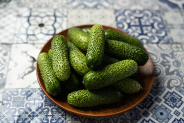 Green cucumbers on a plate, light patterned background, horizontal format
