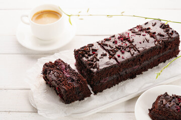 Chocolate cake with cherry, cut into portions, white wooden background, coffee in the foreground