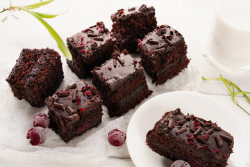 Chocolate cake with cherry, cut into portions, white wooden background, glass with milk