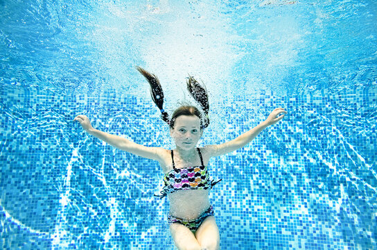 Funny child swims underwater in swimming pool, active little girl jumps, dives and has fun under water, kid fitness and sport on family vacation 

