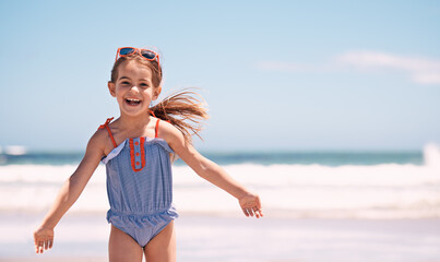 Happy, portrait and little girl playing at the beach for fun holiday, weekend or outdoor summer. Excited female person, child or young kid with smile in happiness for day by the ocean coast in nature