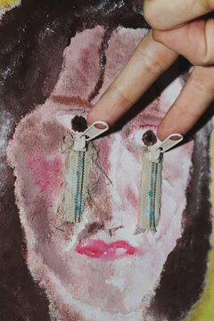 Fingers on painting artwork of a crying woman with zips on face