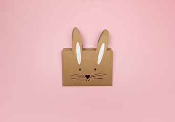 Top view of kraft bunny gift bag on pink background. Creative easter composition, spring, copy space, flat lay.