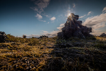 Lava fields on iceland, with magma pillars standing out from the grass. Sun is shining and making a star shaped flare on the sky.