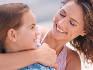 Happy mother, child and hug with love at beach for support, care or bonding on outdoor holiday or weekend in nature. Face of mom and young daughter with smile for embrace by the ocean coast or sea