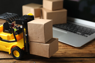 Toy forklift with boxes near laptop on wooden table. Logistics and wholesale concept