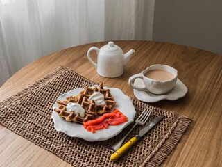 Delicious breakfast, brunch - potato waffles with sour cream and lightly salted salmon and tea with milk on a wooden table