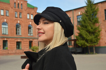 Portrait of a Caucasian blonde girl in a black coat and cap walking along a city street.