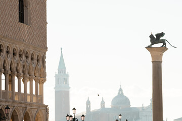 geflügelter Löwe auf monolithischer Säule in Venedig auf der Piazetta im Morgenlicht mit Blick auf Dogenpalast und Insel San Giorgio Maggiore.