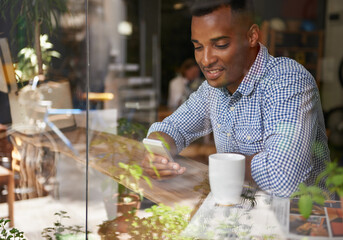 Coffee, window and man with smartphone at cafe for social media, communication and networking. Person, smile and technology in restaurant for texting, message and scrolling on website online