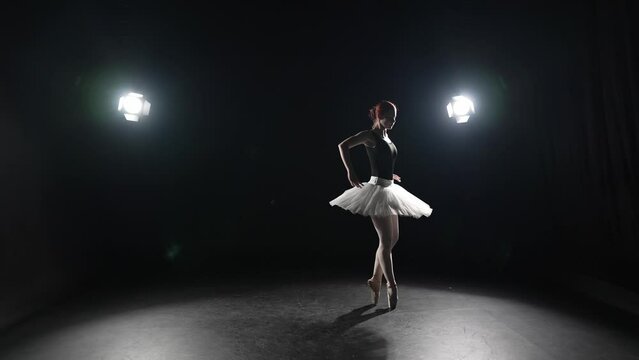 Graceful ballerina dancing in studio. Professional ballet dancer young woman in pointe shoes and white tutu performing dancing elements of classical ballet. Ballet dance studio, sport festive concept.
