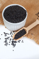 Black sesame seeds with bowl and wooden scoop on white with burlap and copy space