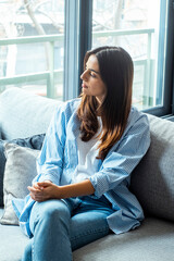 Exhausted frustrated young woman touching forehead, sitting on couch alone, suffering from strong...