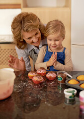 Woman, child and cupcake sprinkles for baking decoration in kitchen for learning support or sweet snack, proud or ingredients. Grandmother, girl and icing recipe at home for teaching, help or happy