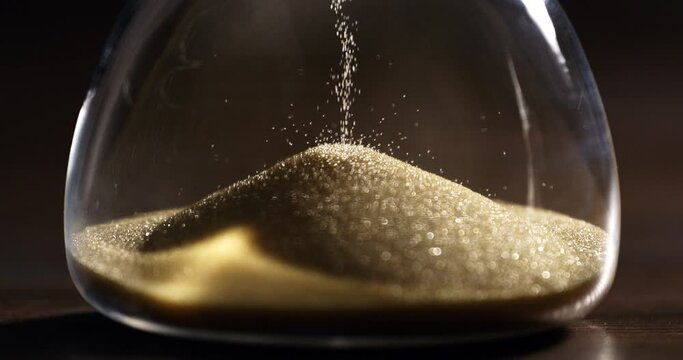 Super slow motion macro of fluid flow of gold sand grains particles running inside hourglass sandglass clepsydra measuring passing time in countdown to deadline at 1000 fps.