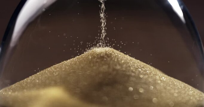 Super slow motion macro of fluid flow of gold sand grains particles running inside hourglass sandglass clepsydra measuring passing time in countdown to deadline at 1000 fps.