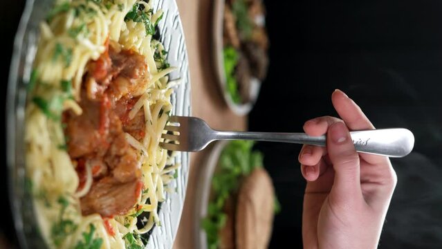 A woman eats spaghetti with goulash in a home-cooking restaurant. Homemade food concept