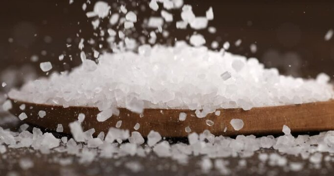 Super slow motion macro of granulated rough crystal himalayan salt grains in wooden plate at 1000 fps.