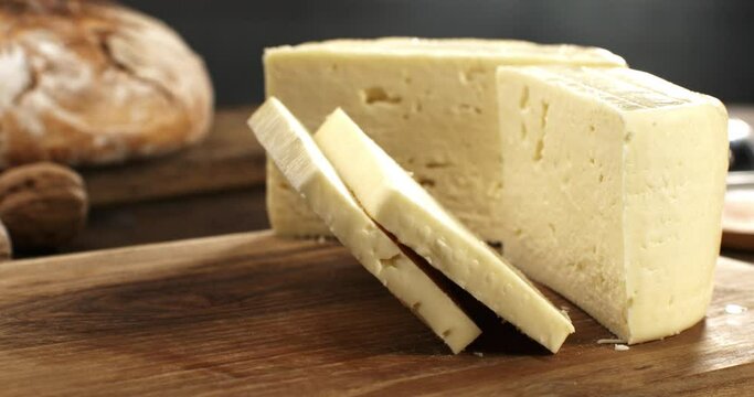 Super slow motion macro of slices traditional italian bio organic toma cheese is falling on rustic wooden chopping board in kitchen of restaurant  or dairy farm at 1000 fps.