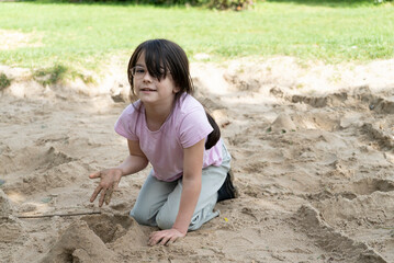 Little girl playing in the sand on the playground in the park.