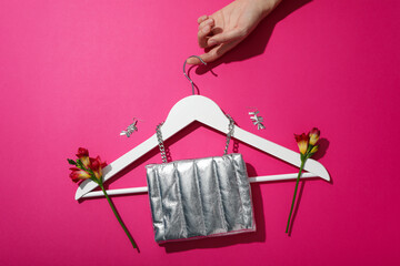Female accessories, hanger in hand and flowers on pink background, top view