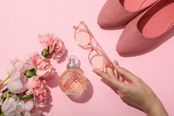 Flowers, female perfume, glasses in hand and shoes on pink background, top view