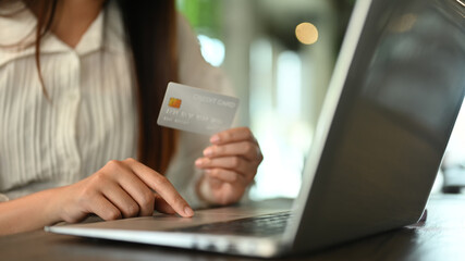 Closeup woman hand holding credit card and typing on laptop, making online shopping or paying bills