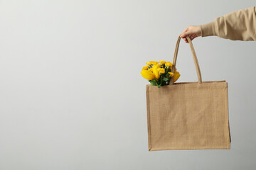 Bag with flowers in female hand on gray background, space for text