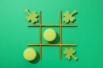 Paper clover leaves, macaroons and cocktail straws on green background, top view
