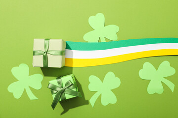 Gift boxes, paper clover leaves and Ireland flag on green background, top view