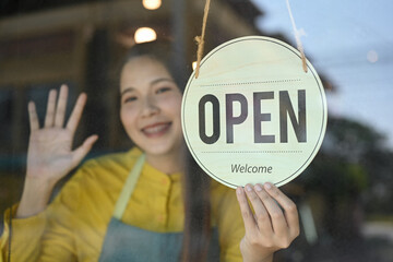 Smiling female small business owner wearing apron turning open sign on the glass door