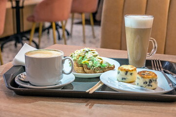 Croissant, cheesecakes and coffee on a tray in a cafe.