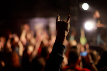 An audience member raises their hand in the “horns” gesture at a lively rock concert,...