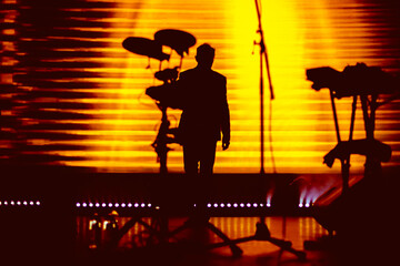 Silhouette of a musician captured against a vibrant orange backdrop during a live performance,...