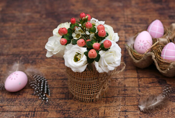 Decorative bouquet of flowers with Easter eggs on wooden background.