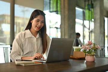 Smiling businesswoman using laptop on wooden table at coffee shop during working remotely