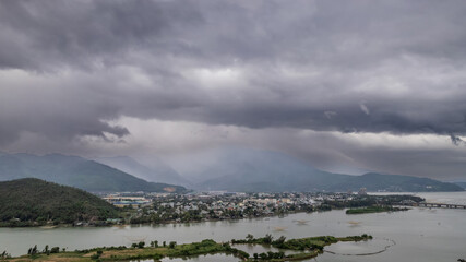 Fototapeta na wymiar Moody panorama of a sprawling town by a river with surrounding mountains, under a dramatic overcast sky, with ample space for text, perfect for environmental or travel-themed content, Earth day concep