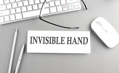INVISIBLE HAND text on paper with keyboard on grey background
