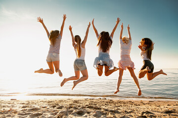Group of happy young girls are having fun and jumping at sunset sea beach