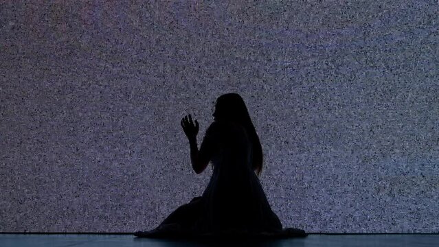 Silhouette against digital television screen. Thriller scene scared trapped woman silhouette sitting on the floor hitting big digital screen with noise.