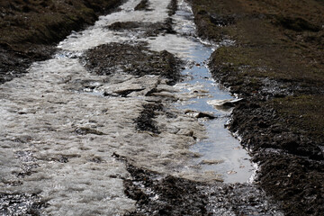 Muddy dirt road with melting ice with puddles and water. Spring landscape in mountains.