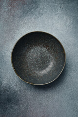 Ceramic dark round textured plate. Close up on gray concrete background. Free space for text.