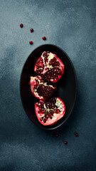 Creative photo, close-up top view of fresh pomegranate pieces on a black stone plate.