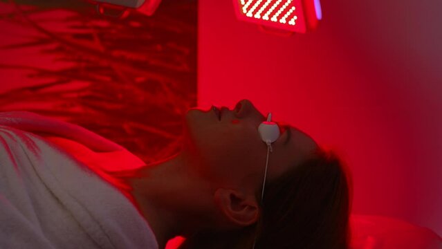 Relaxed female patient undergoes red LED light or RLT therapy for skin rejuvenation at modern innovation aesthetic clinic. Woman client having non-invasive type of phototherapy. Beauty concept.