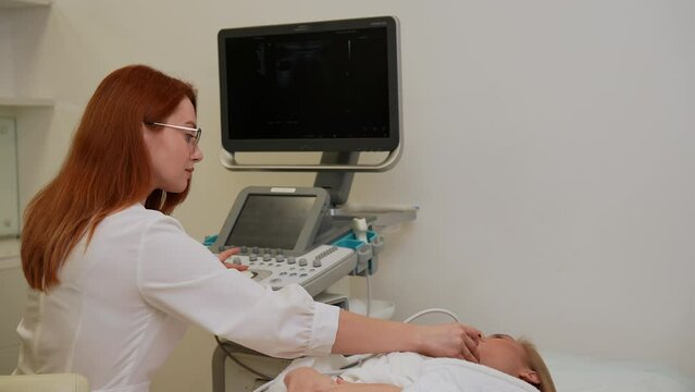 Tracking shot of checkup and scanning of thyroid gland at ultrasound scanner in hospital to young woman patient. Female doctor runs ultrasound sensor over patient neck. Diagnostic procedure in clinic.