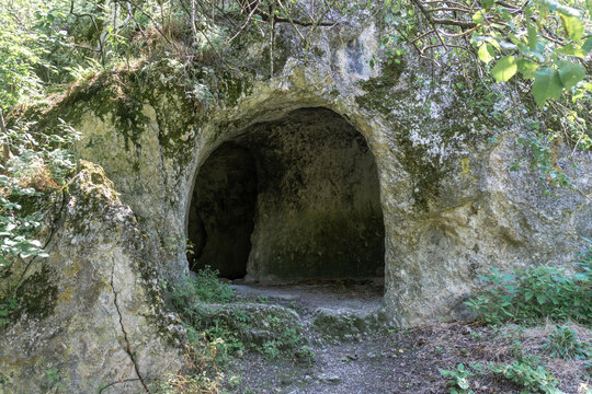 Entrance to the artificial cave in the rock surrounded by branches and grass. One of the entrances and exits of the fortress.