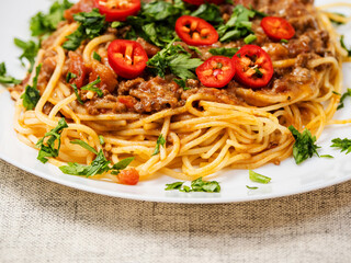 Spaghetti Bolognese dish with pasta, red sauce, minced beef, red peppers and green fresh herbs on white plate and light color table cloth. High quality products in a tasty Italian style dish.