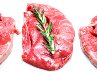 Three uncooked boneless lamb leg steak with fresh rosemary herb on white background. Premium high quality meat product of agriculture industry. Butcher craft and skill. Food supply chain.